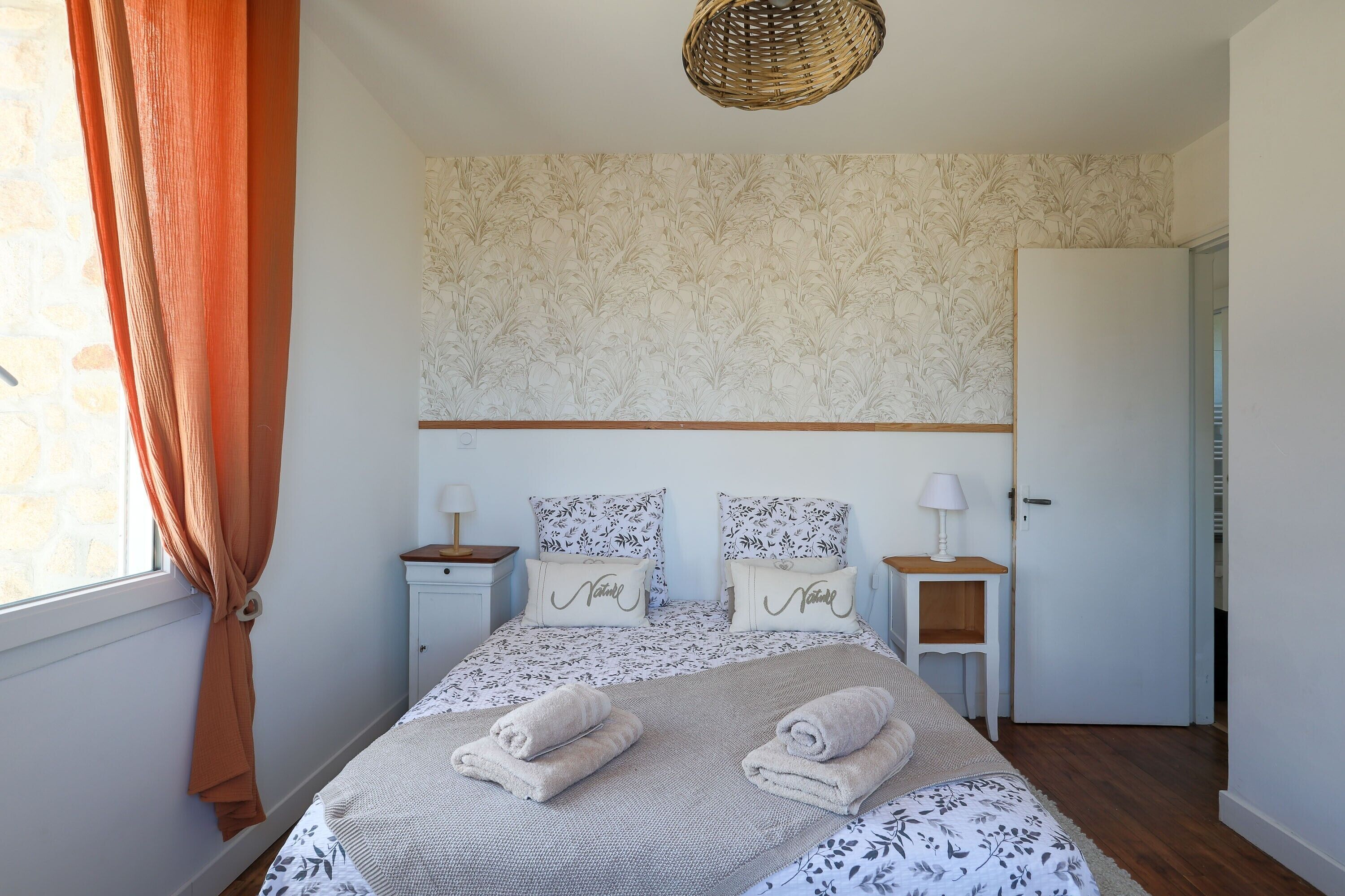 A bedroom with a bed, two nightstands, a door, and a window with curtains.