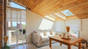 A cozy room with a wooden ceiling, a sofa, a table, and a window with a view.