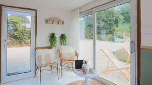 A room with a sliding glass door leading to an outdoor area, a wicker chair, a small table with a jar and a cup, and a laptop on the table.