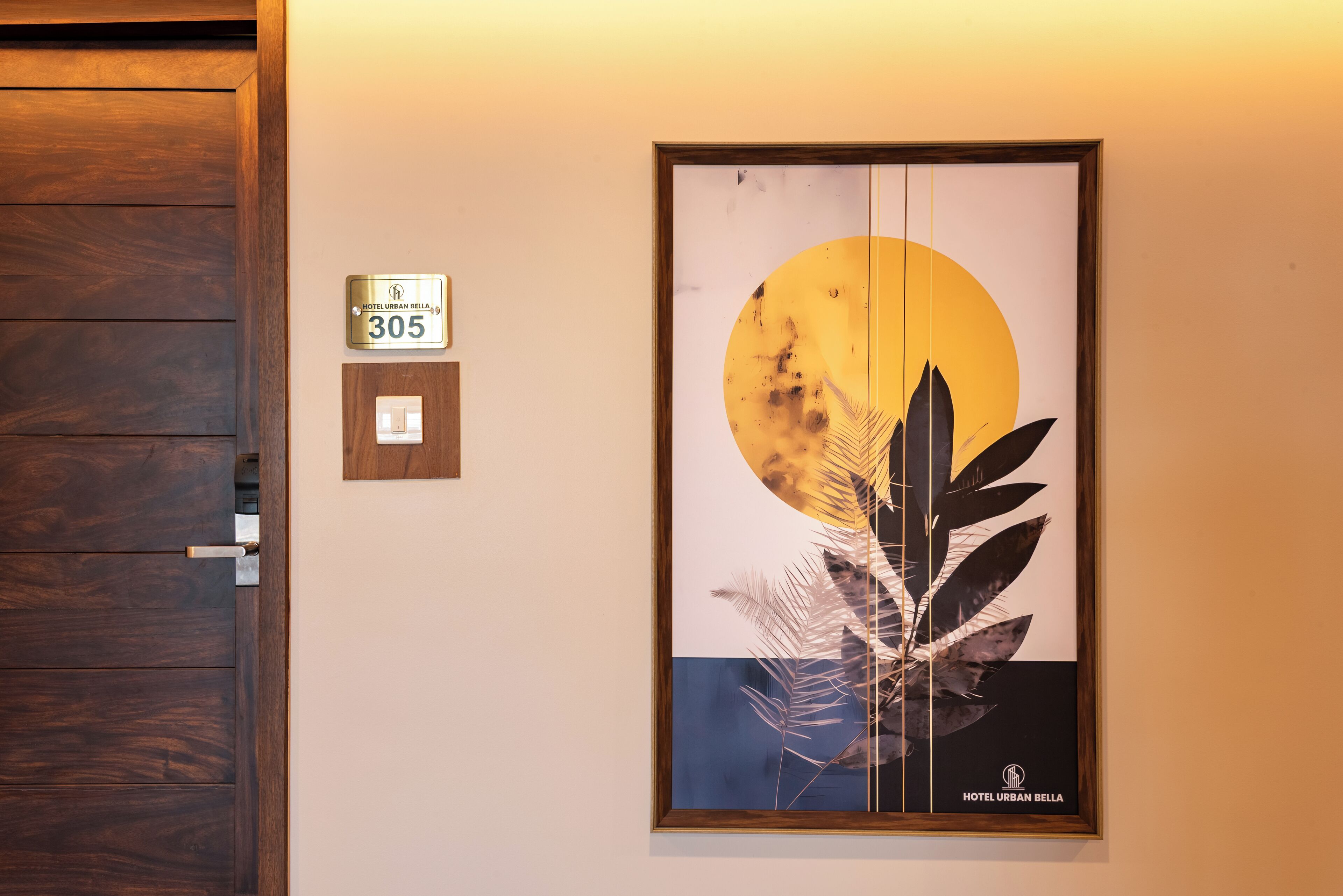 A hotel room with a wooden door, a wall-mounted sign indicating room number 305, and a framed artwork depicting a sun and foliage.