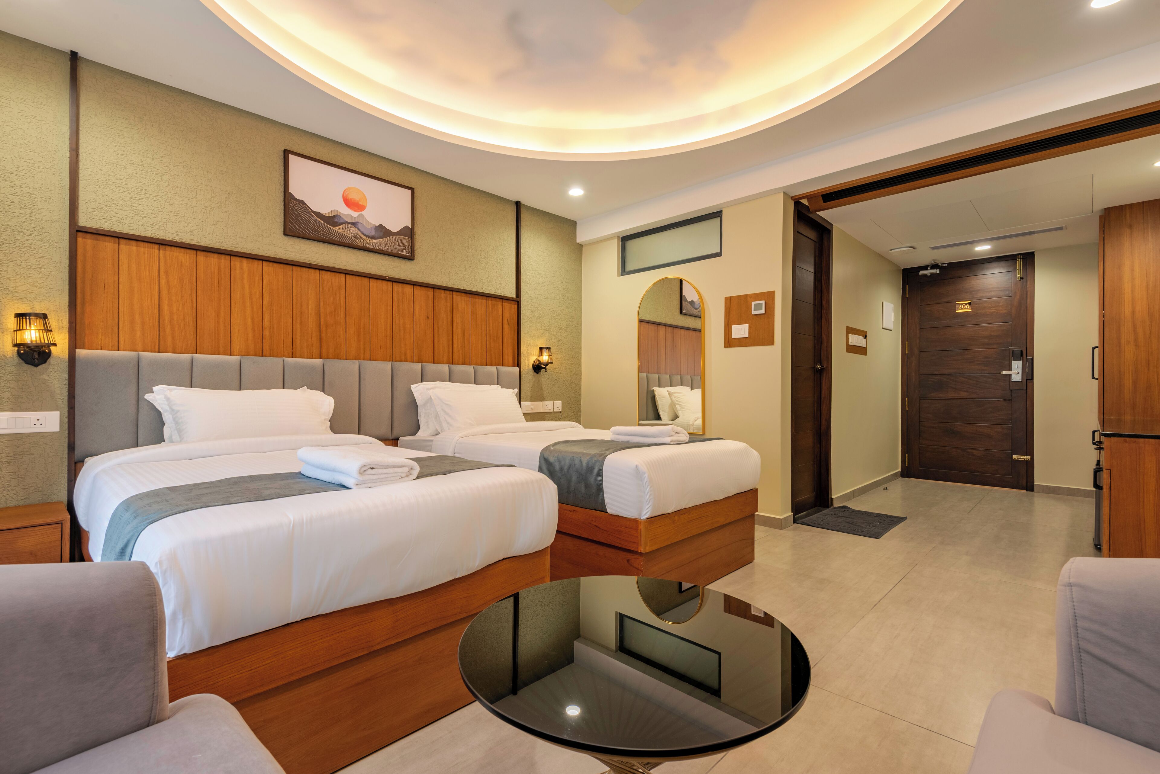 A hotel room with two beds, a round table, and a view of the hallway.