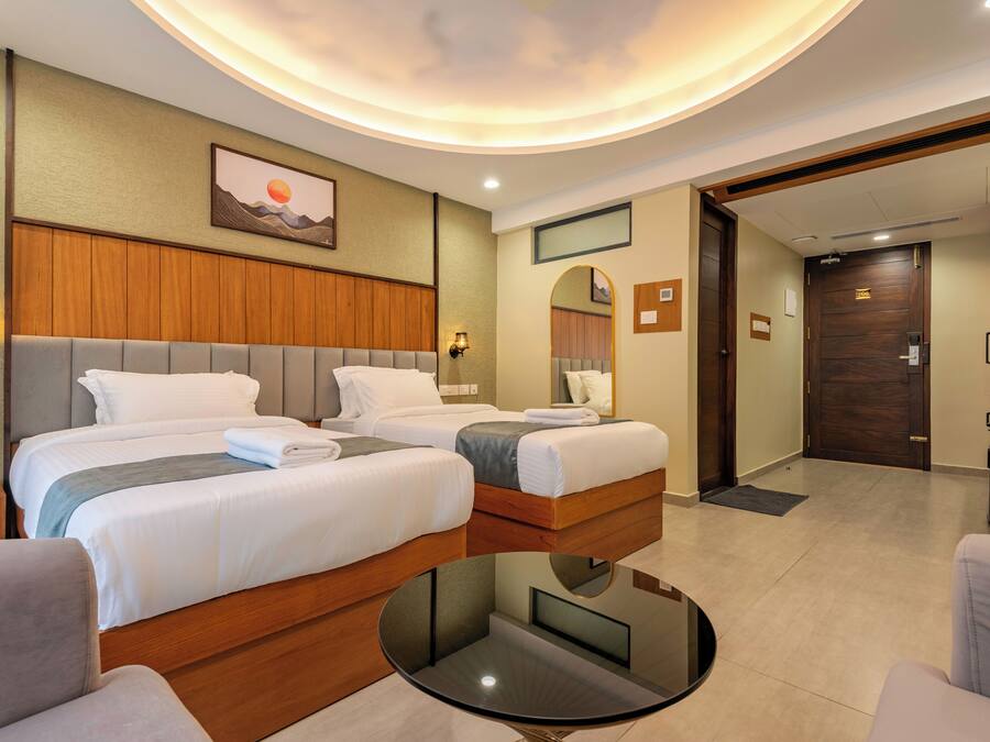 A hotel room with two beds, a round table, and a view of the hallway.