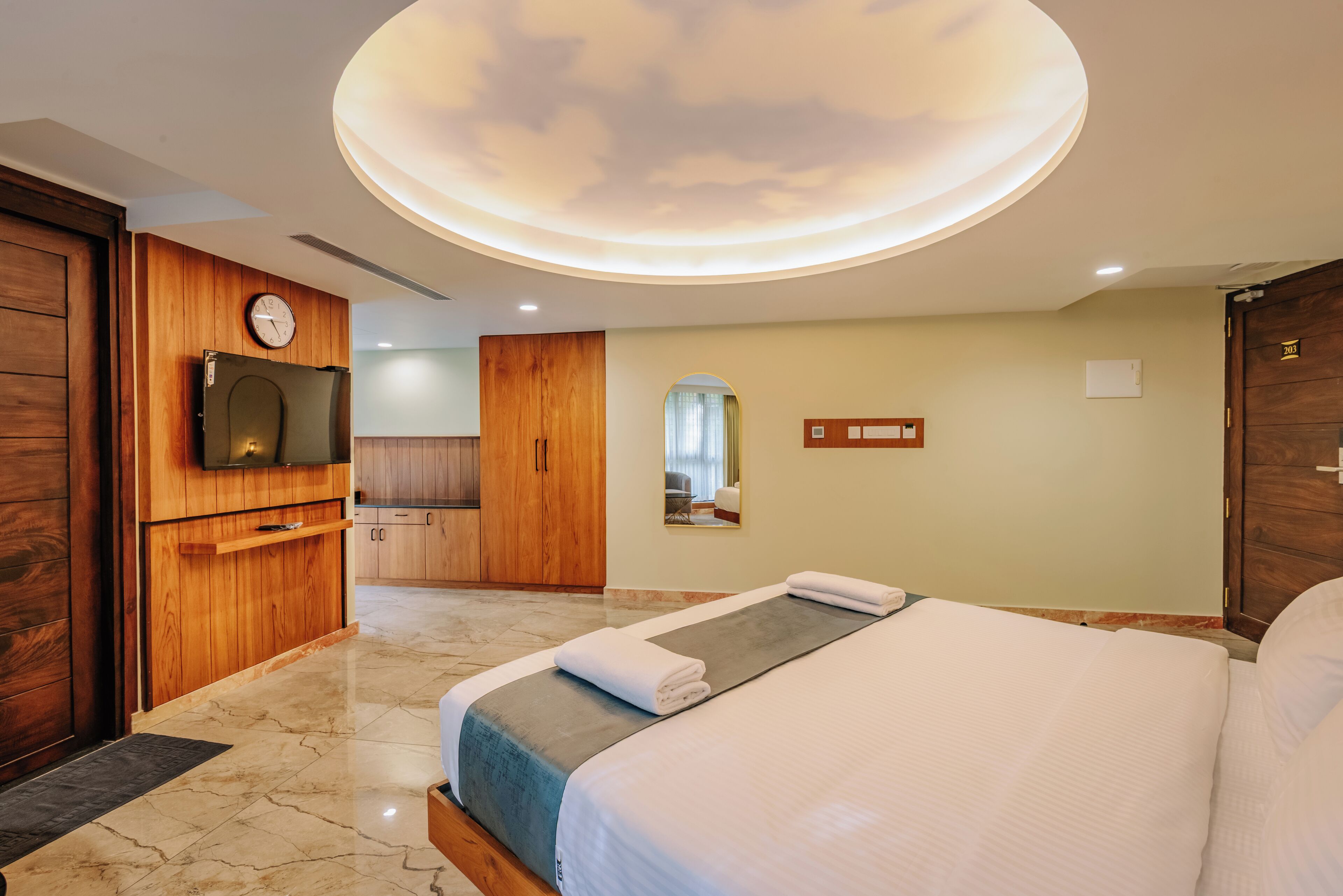 A modern hotel room with a large bed, wooden wardrobe, a television, and a ceiling with a cloud design.