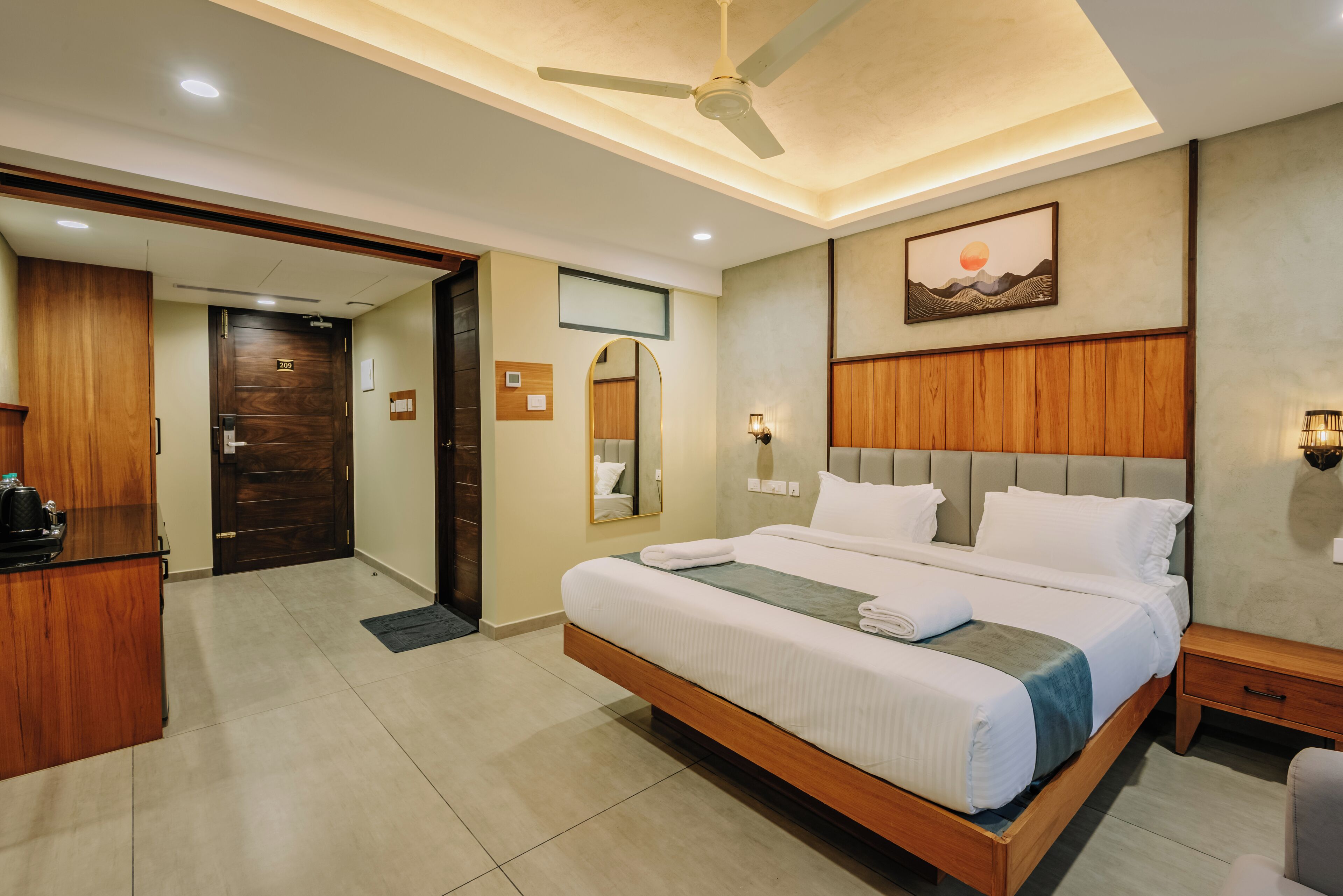 A hotel room with a large bed, a wooden headboard, a ceiling fan, a nightstand, and a desk with a chair.