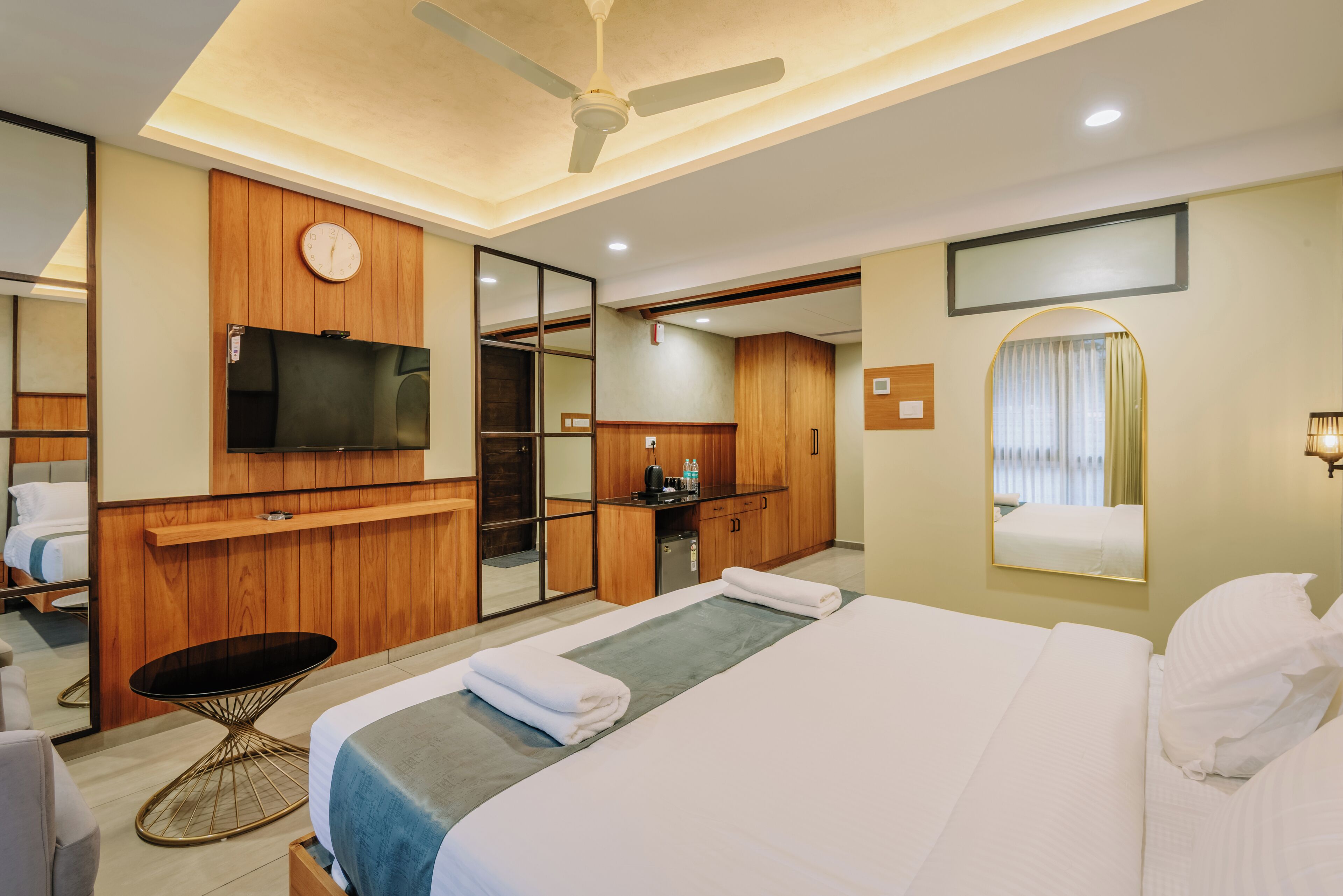 A hotel room with a large bed, a TV mounted on the wall, a desk with a chair, and a mirror.