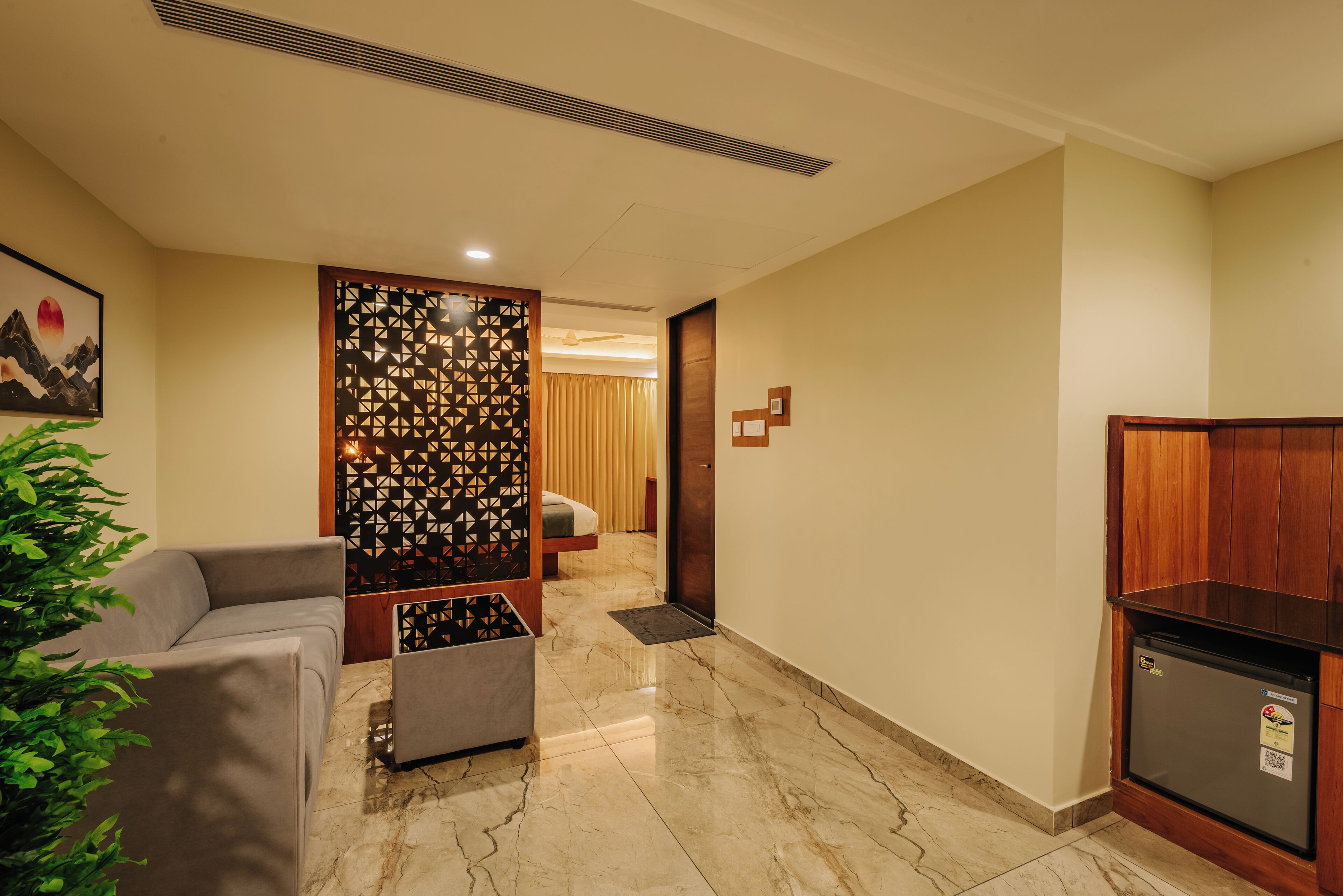 A hotel lobby with a sofa, a decorative partition, a refrigerator, and a door leading to another room.