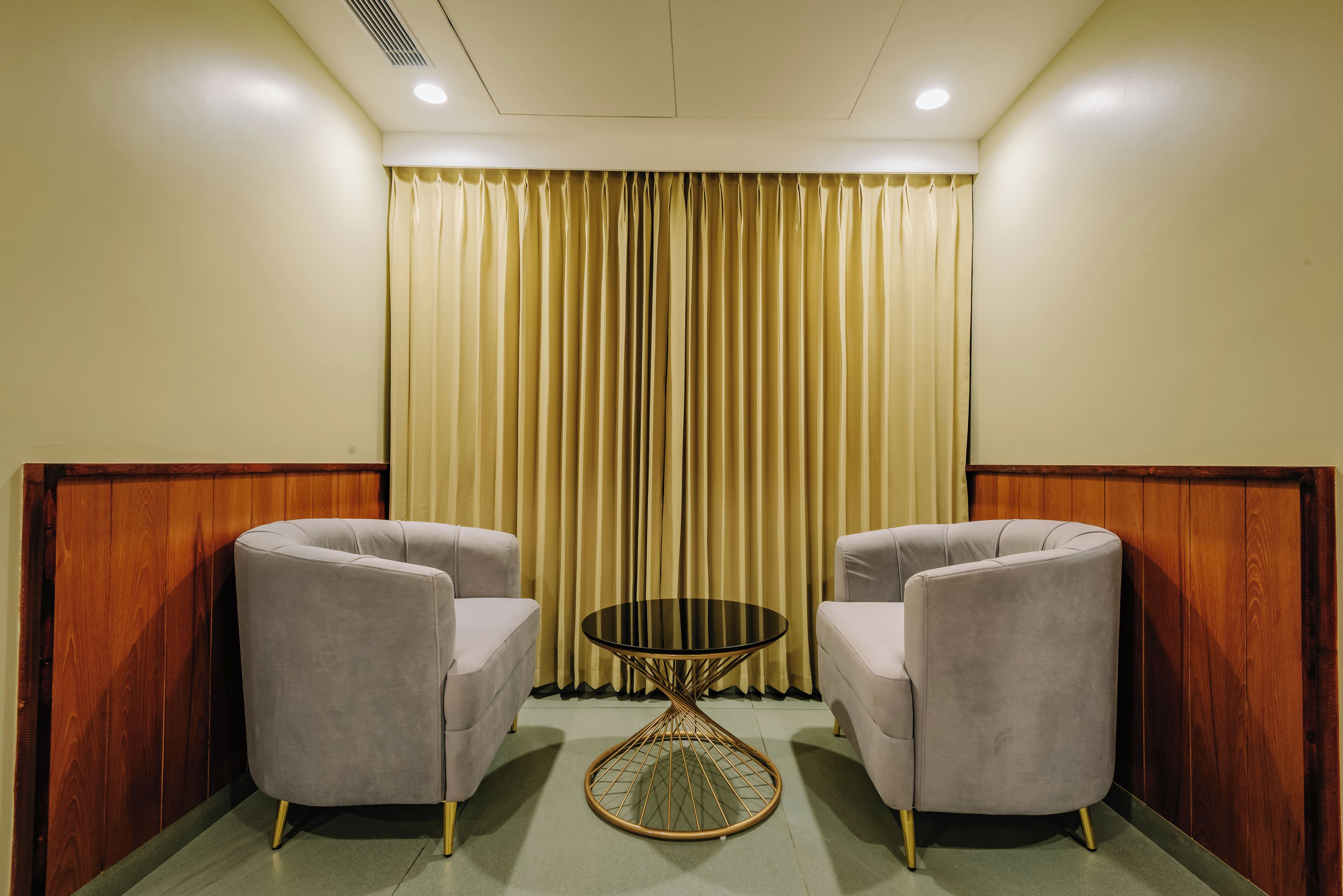 A room with two grey armchairs, a round table, and a curtain backdrop.