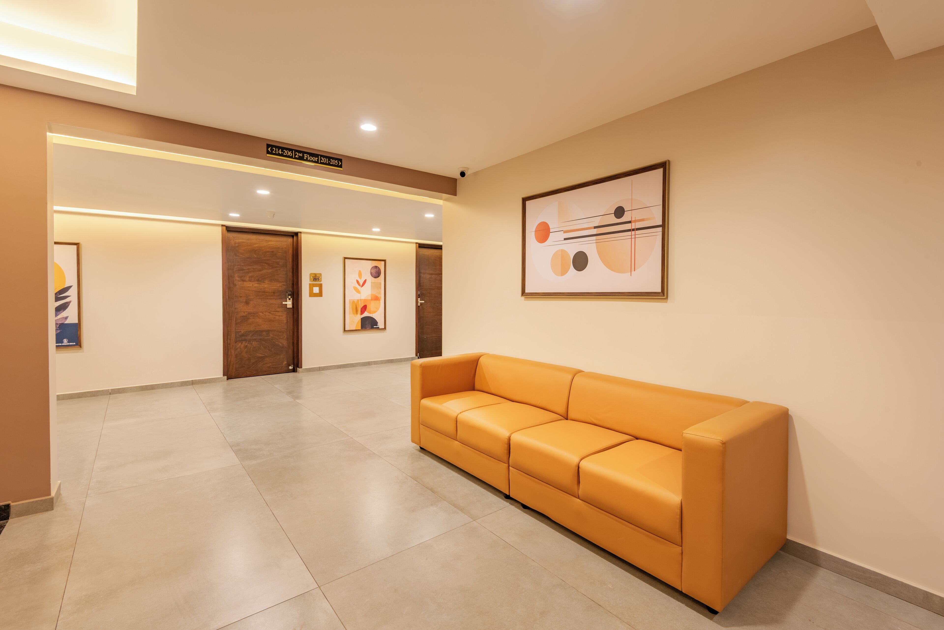 A hotel lobby with a reception desk, a waiting area with a sofa, and a corridor leading to doors.