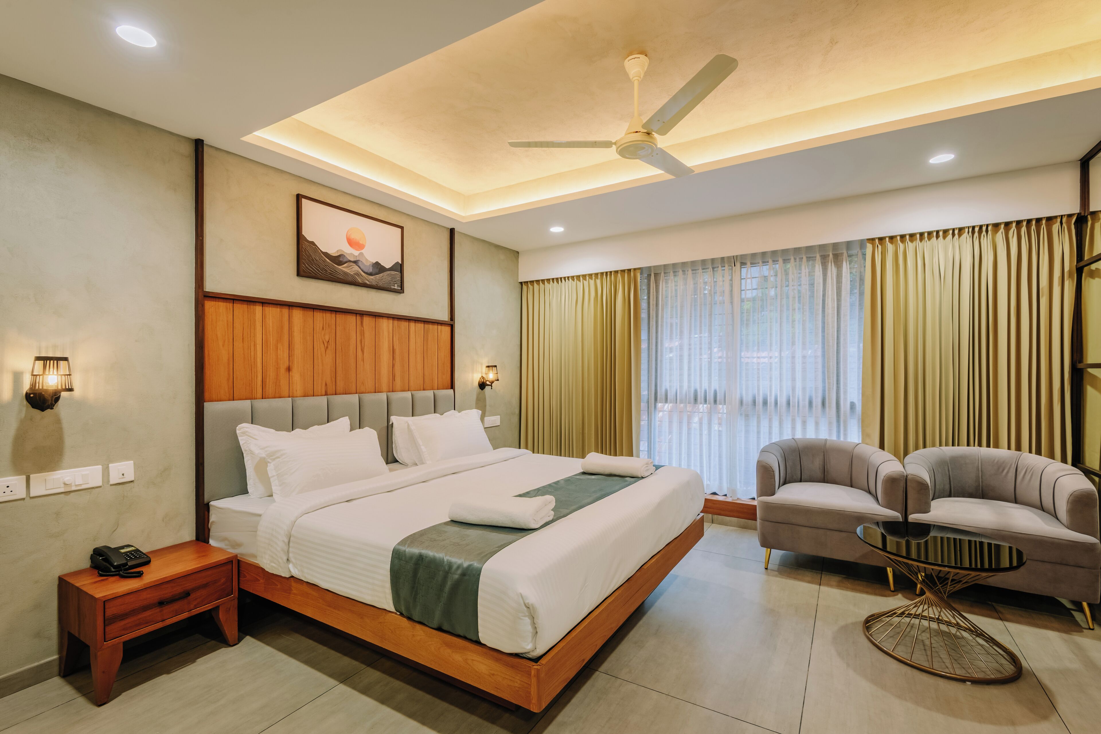 Una habitación de hotel con una cama, un sofá, una mesita, un ventilador de techo y un cuadro en la pared.