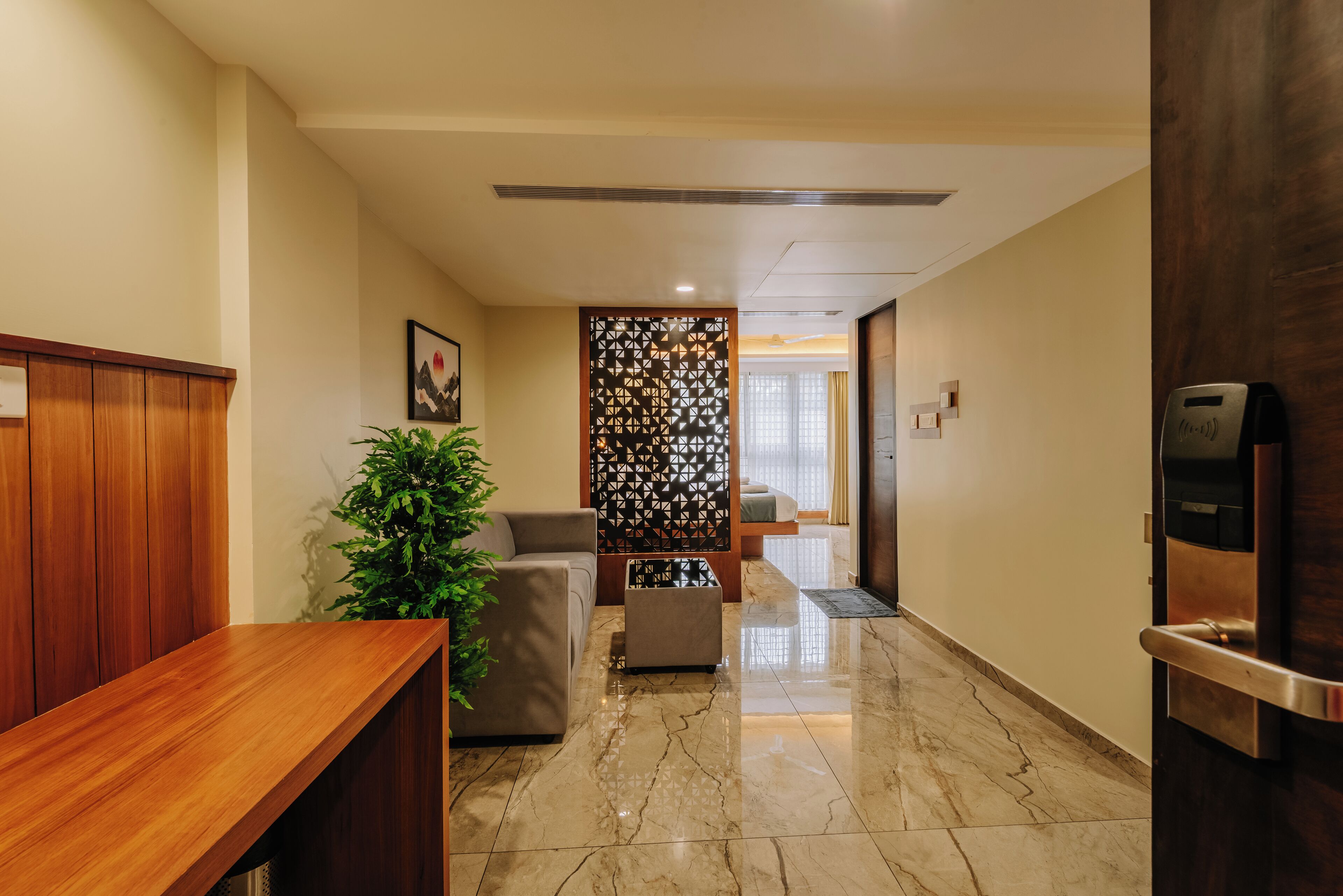 A reception area with a wooden reception desk, a potted plant, a seating area with a sofa and ottoman, a decorative wall panel, and a door with a keycard reader.