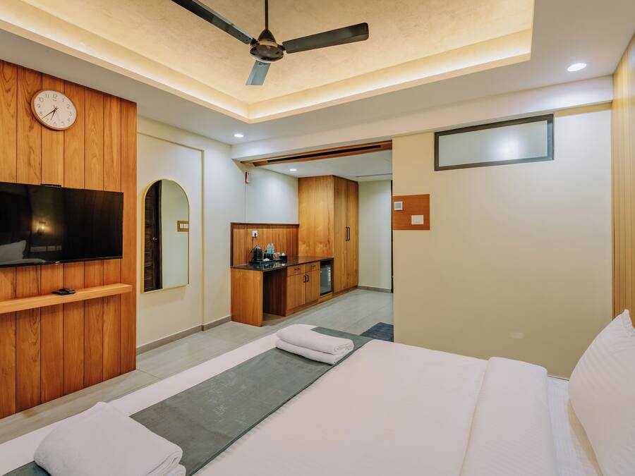 Habitación de hotel con cama, televisor, ventilador de techo, armario de madera, zona de cocina y espejo.