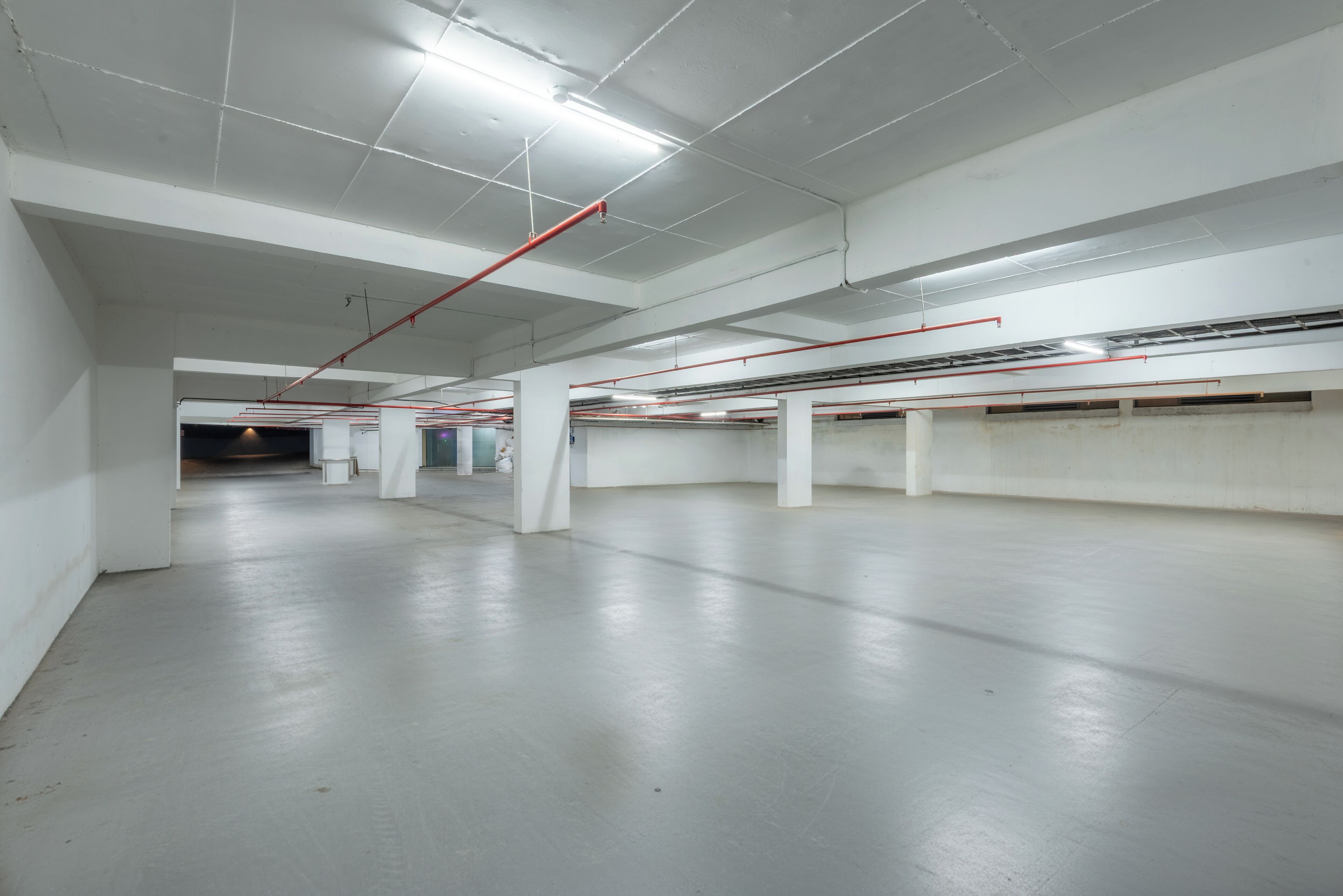 A spacious indoor parking area with white walls and floors, featuring multiple parking bays and overhead lighting.