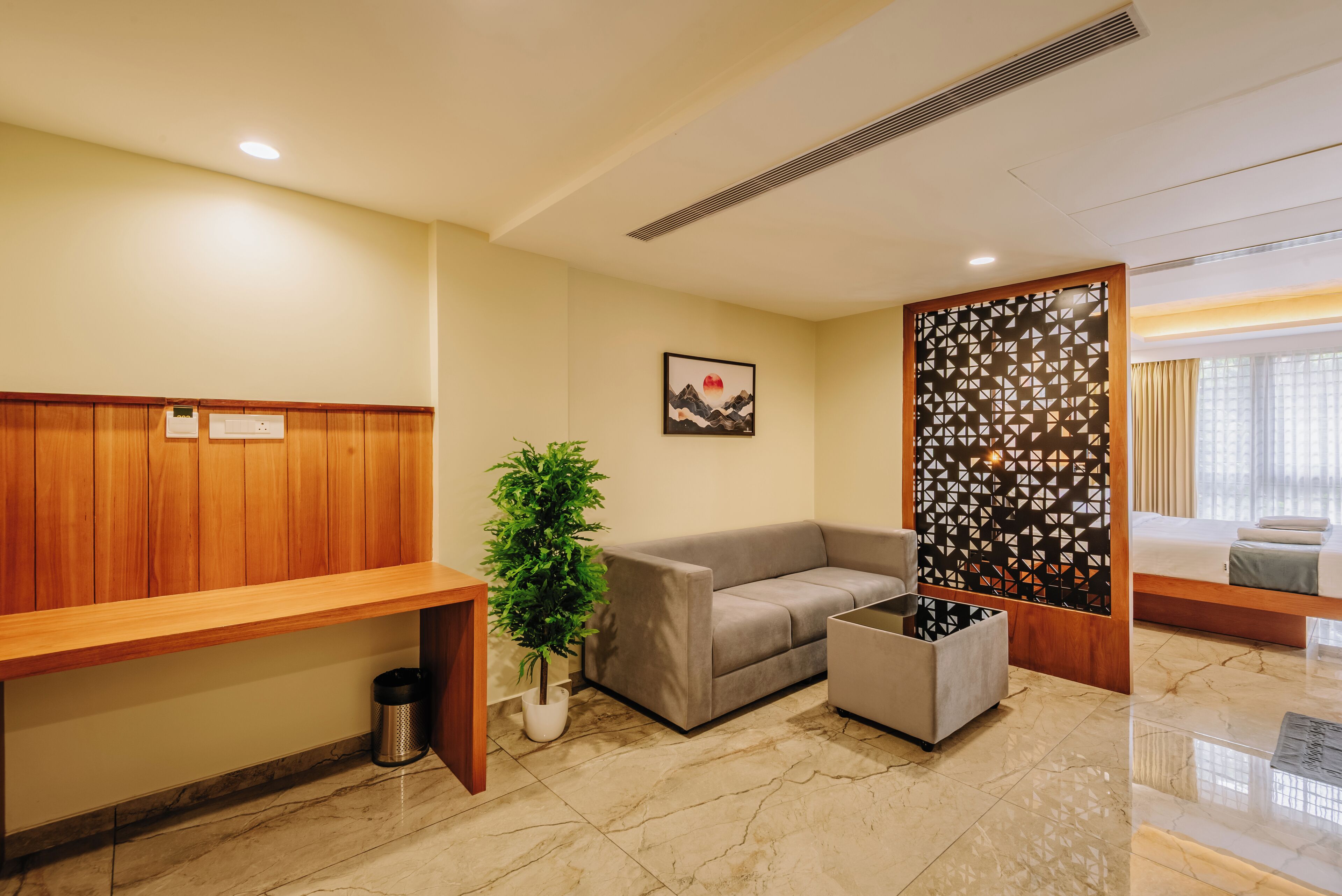 Uma área de recepção com um banco de madeira, um sofá cinzento, um vaso de planta e um painel decorativo na parede.