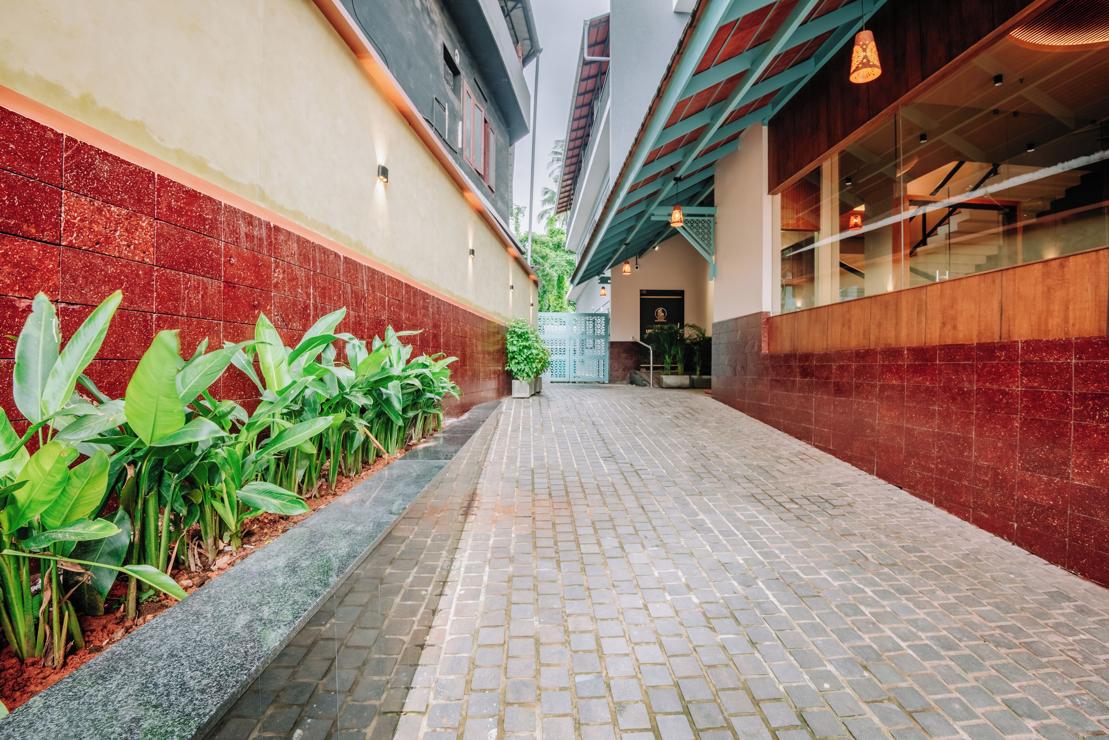 A narrow, paved corridor with red-tiled walls and a row of green plants on one side.