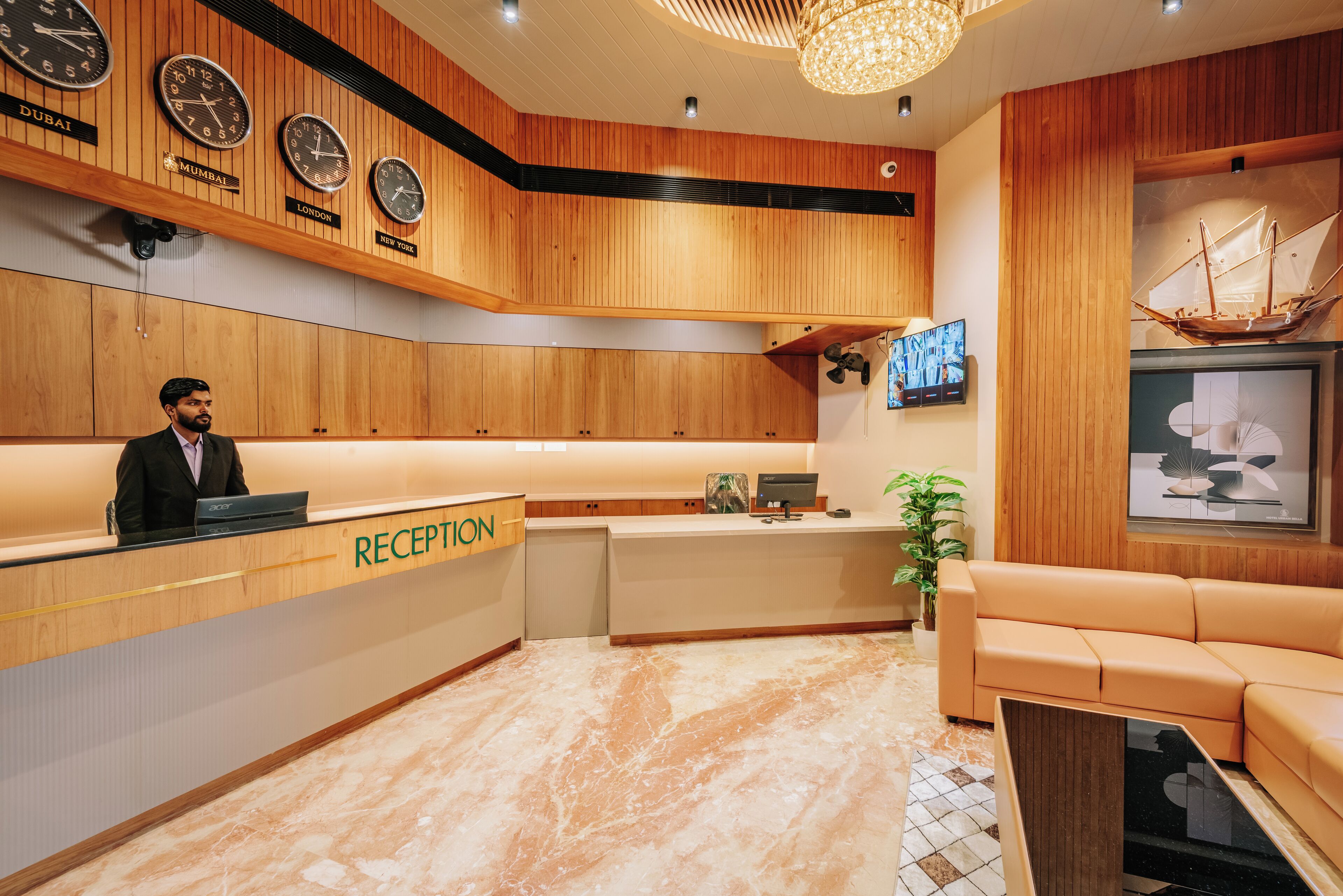 A reception area with wooden paneling, clocks displaying times from Dubai, Mumbai, London, and New York, a reception desk, a sofa, and a ship model on the wall.