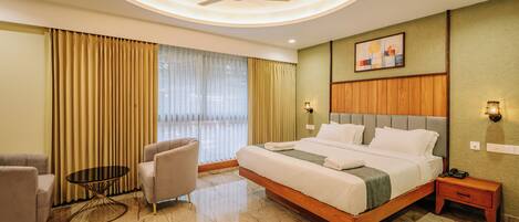 Habitación de hotel con una cama grande, una mesa redonda, dos sillones, un ventilador de techo y un cuadro en la pared.