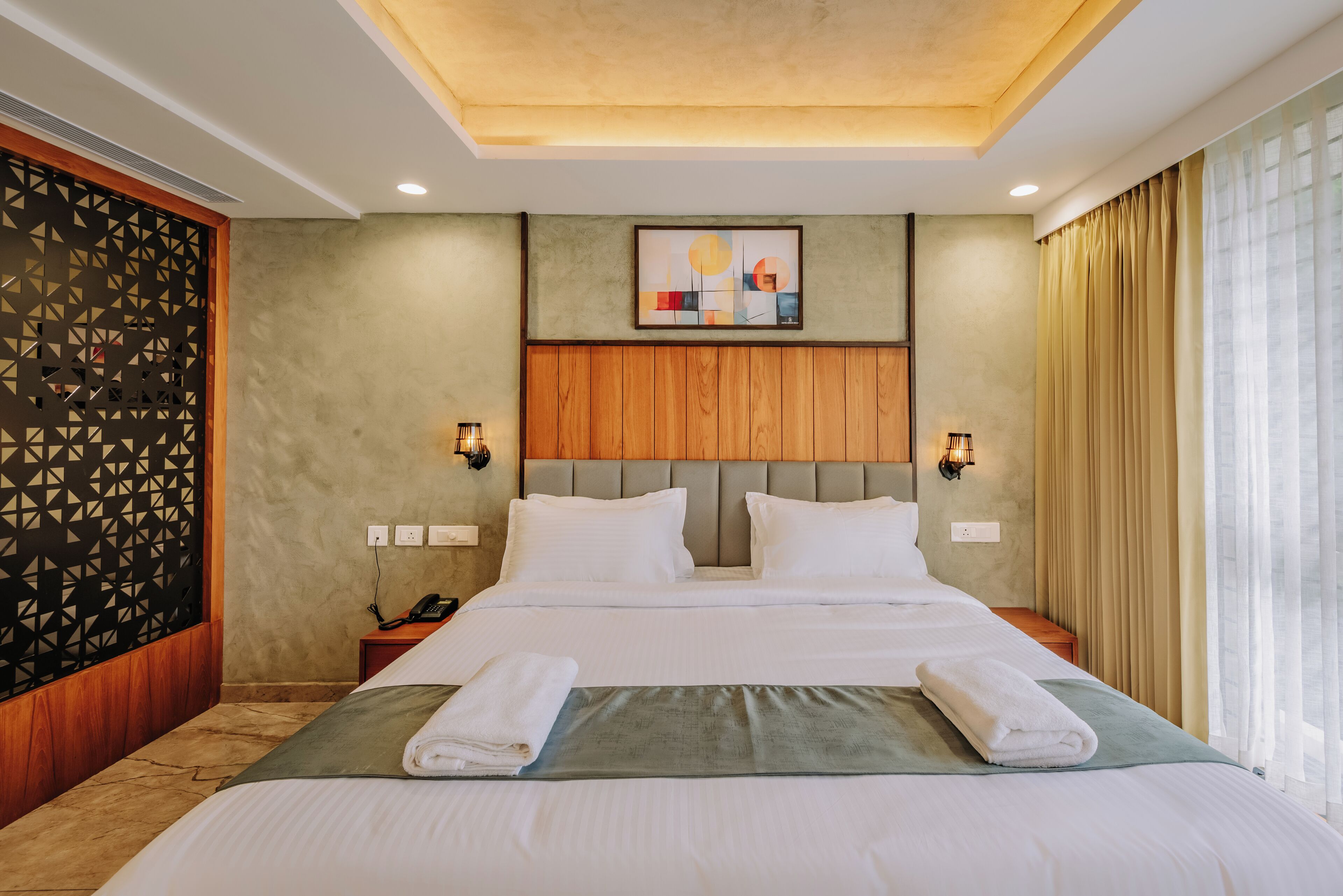 A hotel room with a large bed, two bedside tables, a wall-mounted phone, and a painting above the bed.
