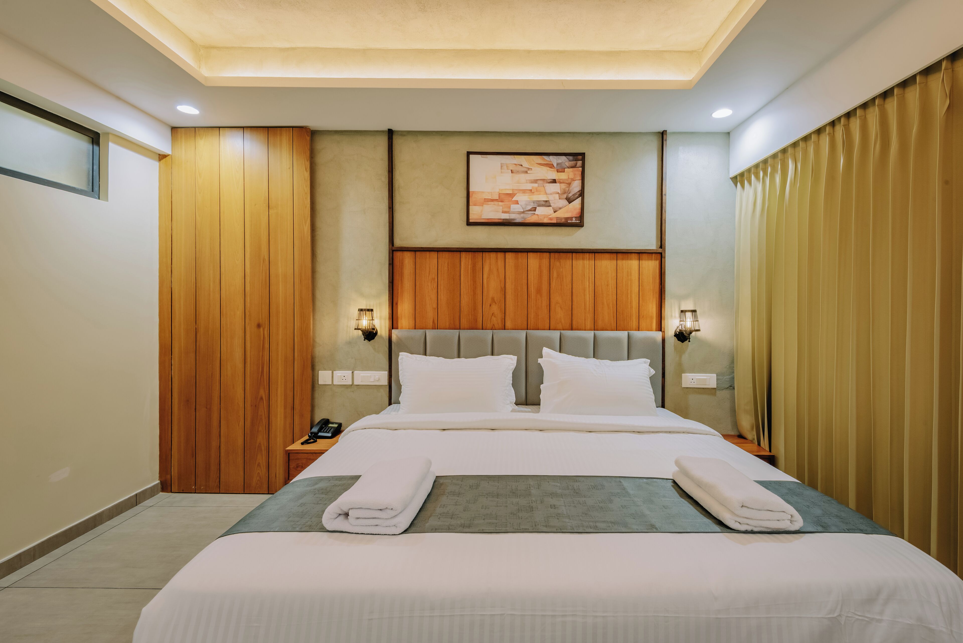 A hotel room with a large bed, wooden panel walls, a ceiling light, and a painting on the wall.
