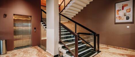 A modern interior with a marble floor, a staircase with glass railings, and an elevator.