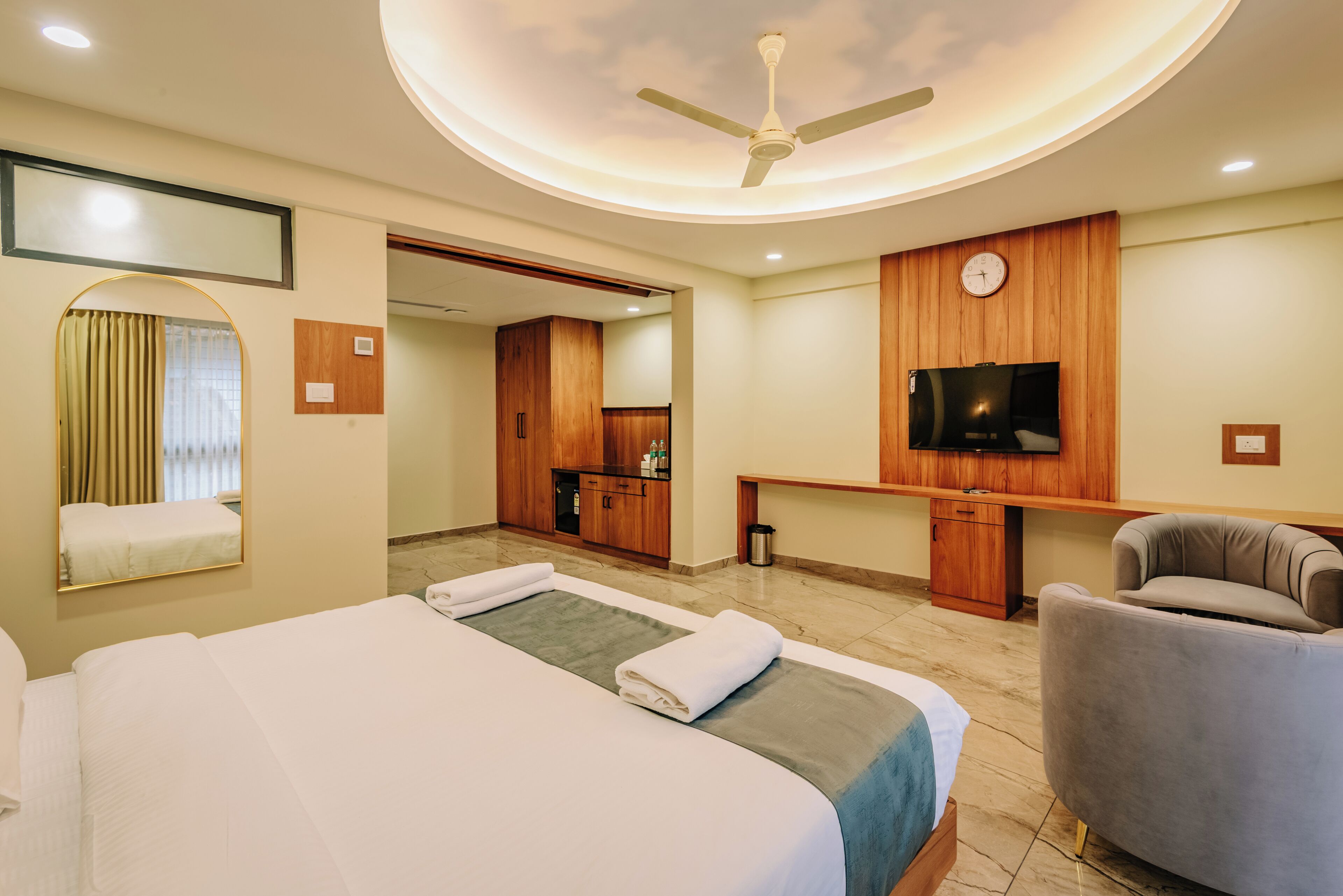 A hotel room with a bed, a chair, a TV, and a ceiling fan.