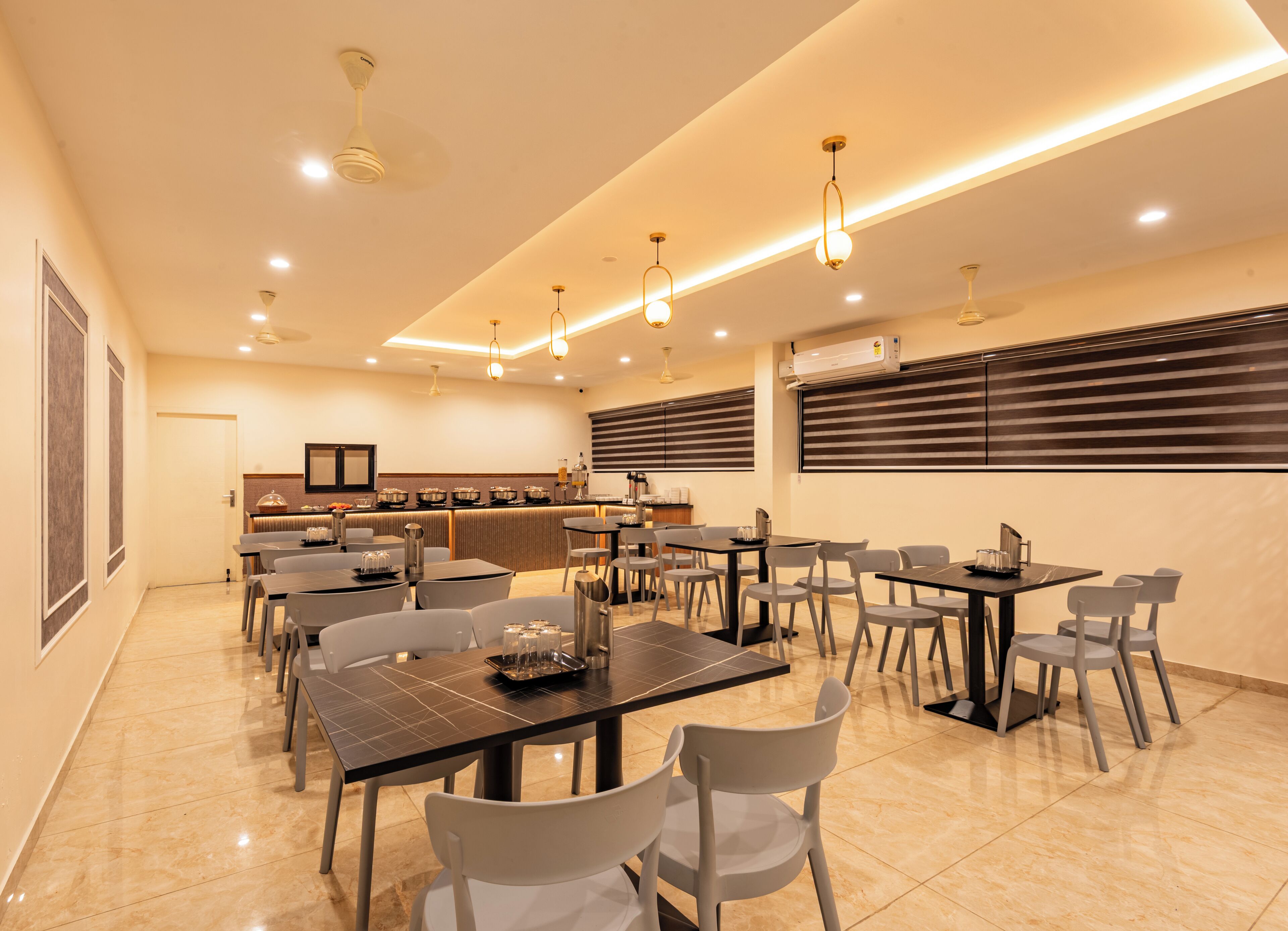 A modern dining area with multiple tables and chairs, a kitchen counter, and ceiling fans.