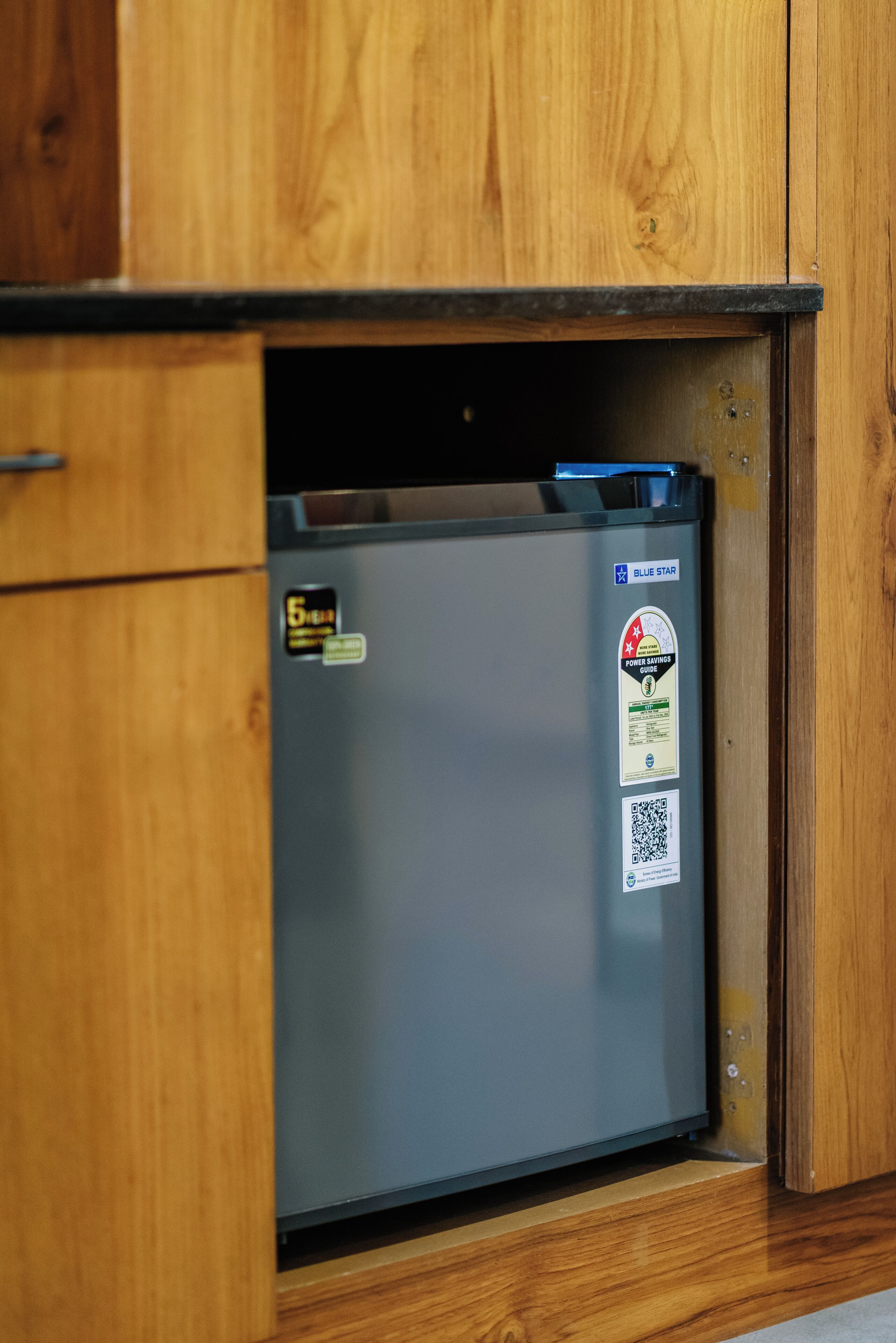 Un refrigerador compacto con un adhesivo azul y un código QR, ubicado en un gabinete de madera.