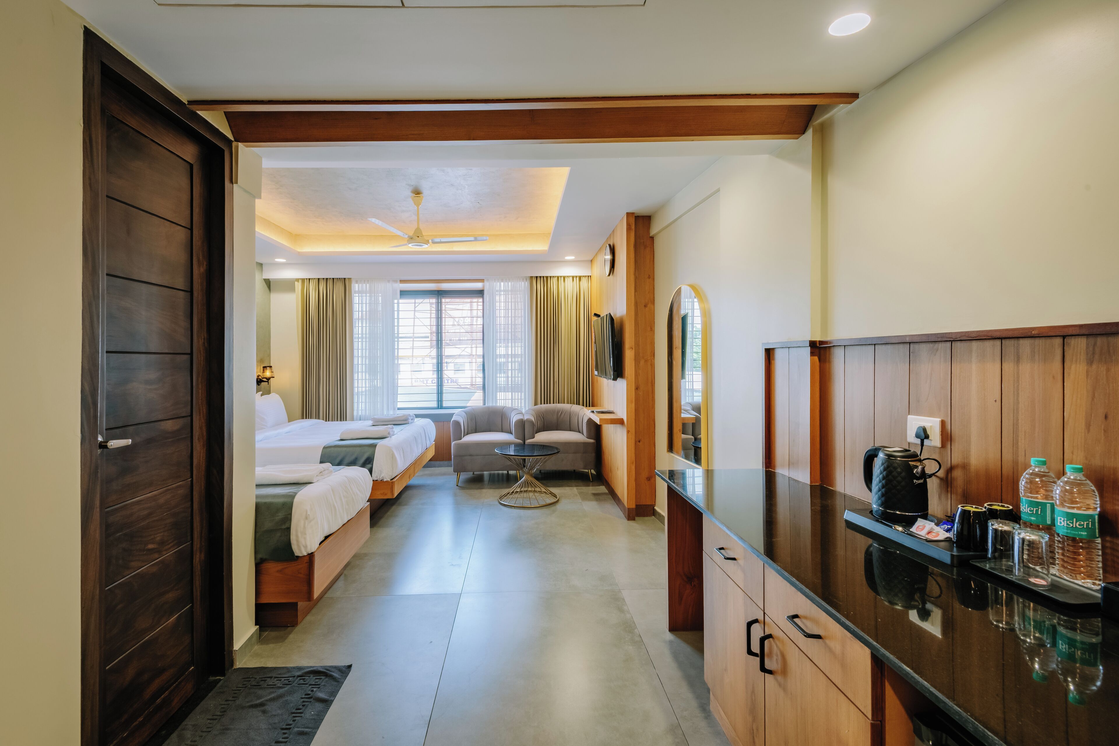 A hotel room with a bed, two bedside tables, a sofa, a small table, a mirror, a coffee maker, and a minibar.