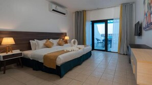 A hotel room with a bed, a desk, a chair, a TV, and a balcony with a view. - La Fontain lagoon resort  (Jeddah)
