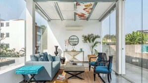 Ein modernes Wohnzimmer mit grauem Sofa, blauem Sessel und Couchtisch, mit Glaswand und Kunst am Decken.