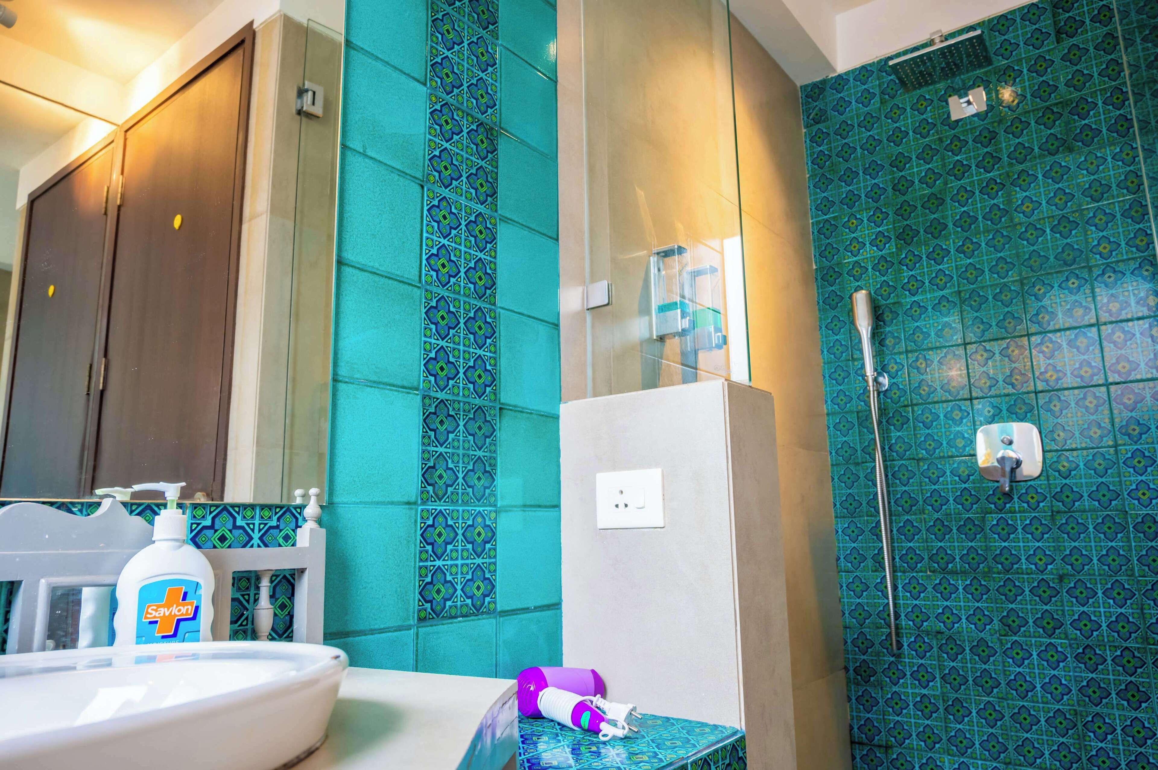 A bathroom with a sink, a bottle of Savlon soap, a purple towel, and a shower area with a blue patterned tile wall.