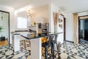 A modern kitchen with a central island, bar stools, and a geometric patterned floor. - Coastal Grandeur by Da Alohas (Nerul)