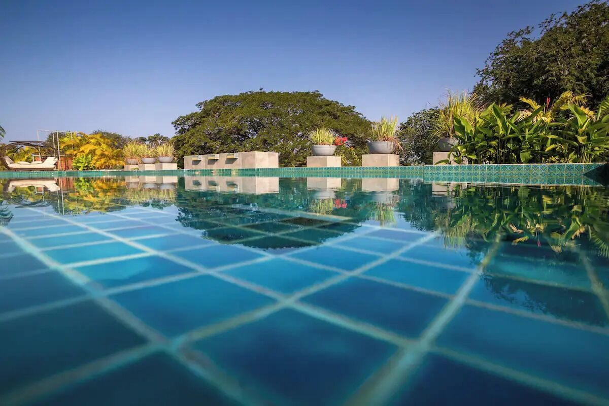 A clear blue pool with a tiled edge, surrounded by lush greenery and a boat.