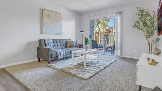 A modern living room with a grey sofa, a white coffee table, and a large window with a view of a balcony.