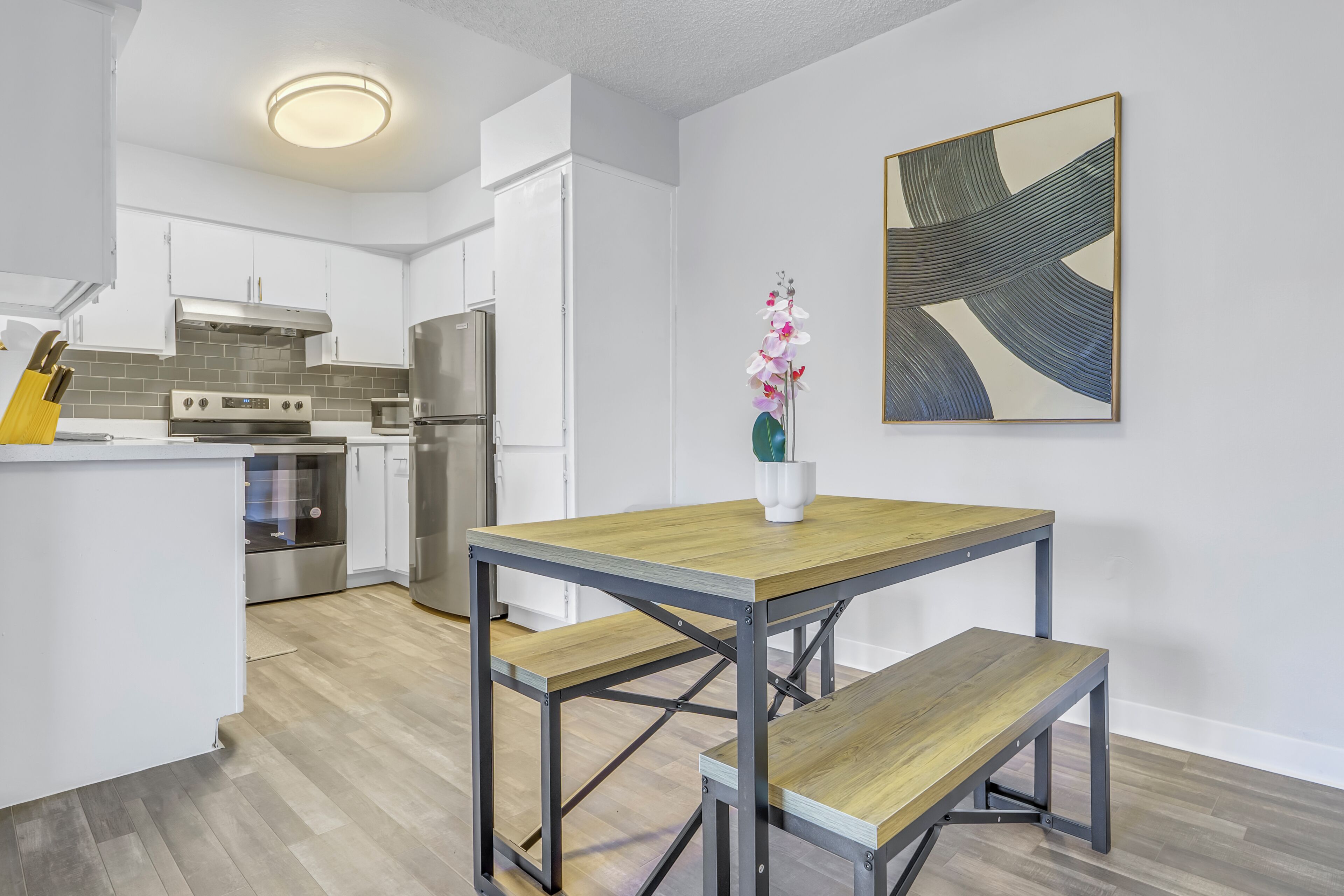Una cocina moderna con armarios blancos, electrodomésticos de acero inoxidable y una mesa de comedor de madera con bancos.
