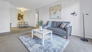 A modern living room with a grey sofa, a white coffee table, and a blue rug. There is a floor lamp and a painting on the wall.