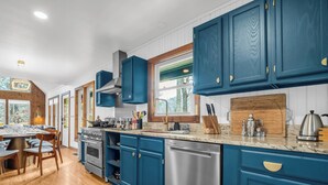 A modern kitchen with blue cabinets, stainless steel appliances, and a wooden dining area. - Luxury•5 Kings•MTN Views and Lake Access•FirePit•EVCharger•PoolTable (Lake Lure)
