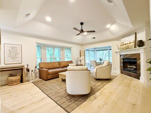 Un salón amplio con un sofá de cuero marrón, un sillón blanco y una chimenea.