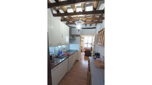 A narrow kitchen with wooden beams, white cabinets, and a wooden floor. - Eras House (Nigüelas)