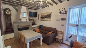 A cozy living room with a fireplace, a sofa, a dining table, and a TV mounted on the wall. - Eras House (Nigüelas)