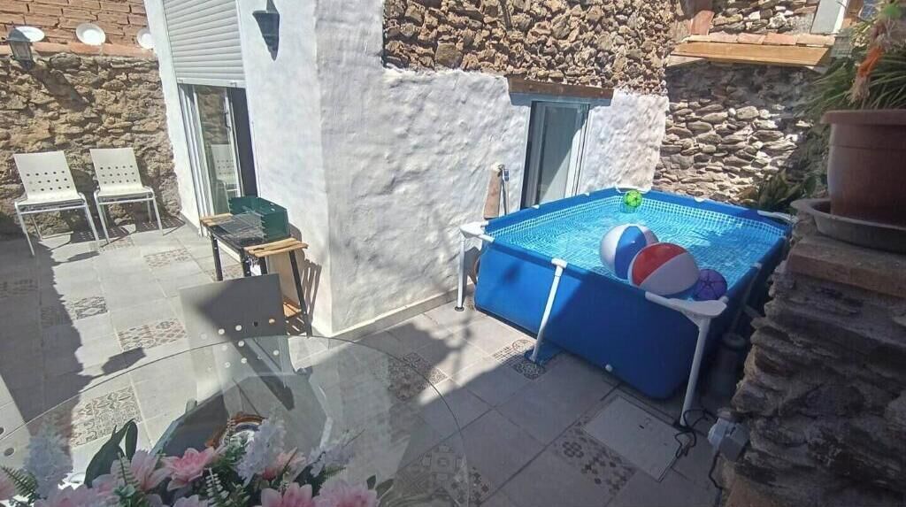 Zwembad met een blauwe afdekking, omgeven door stenen muren en een glazen tafel met stoelen.