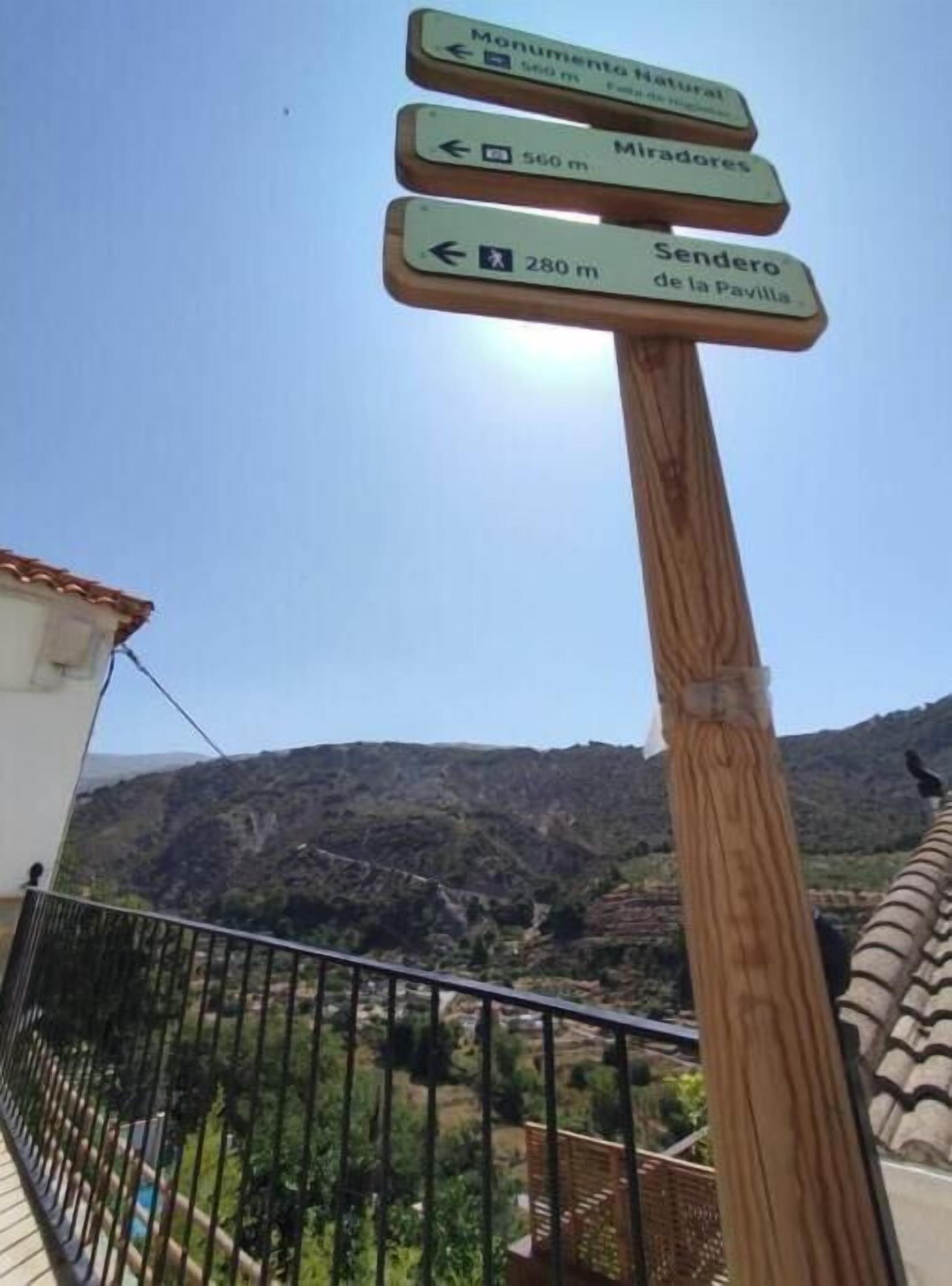 A wooden signpost with directional signs indicating distances to 'Monumento Natural,' 'Miradores,' and 'Sendero de la Pavilla.'