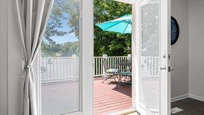 Een uitzicht door een deur naar een terras met een tafel en stoelen, een blauwe parasol en een witte hek.