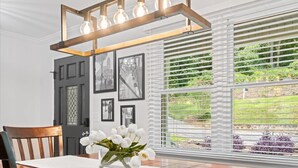 Een eethoek met een houten tafel, witte bloemen en een moderne lamp.