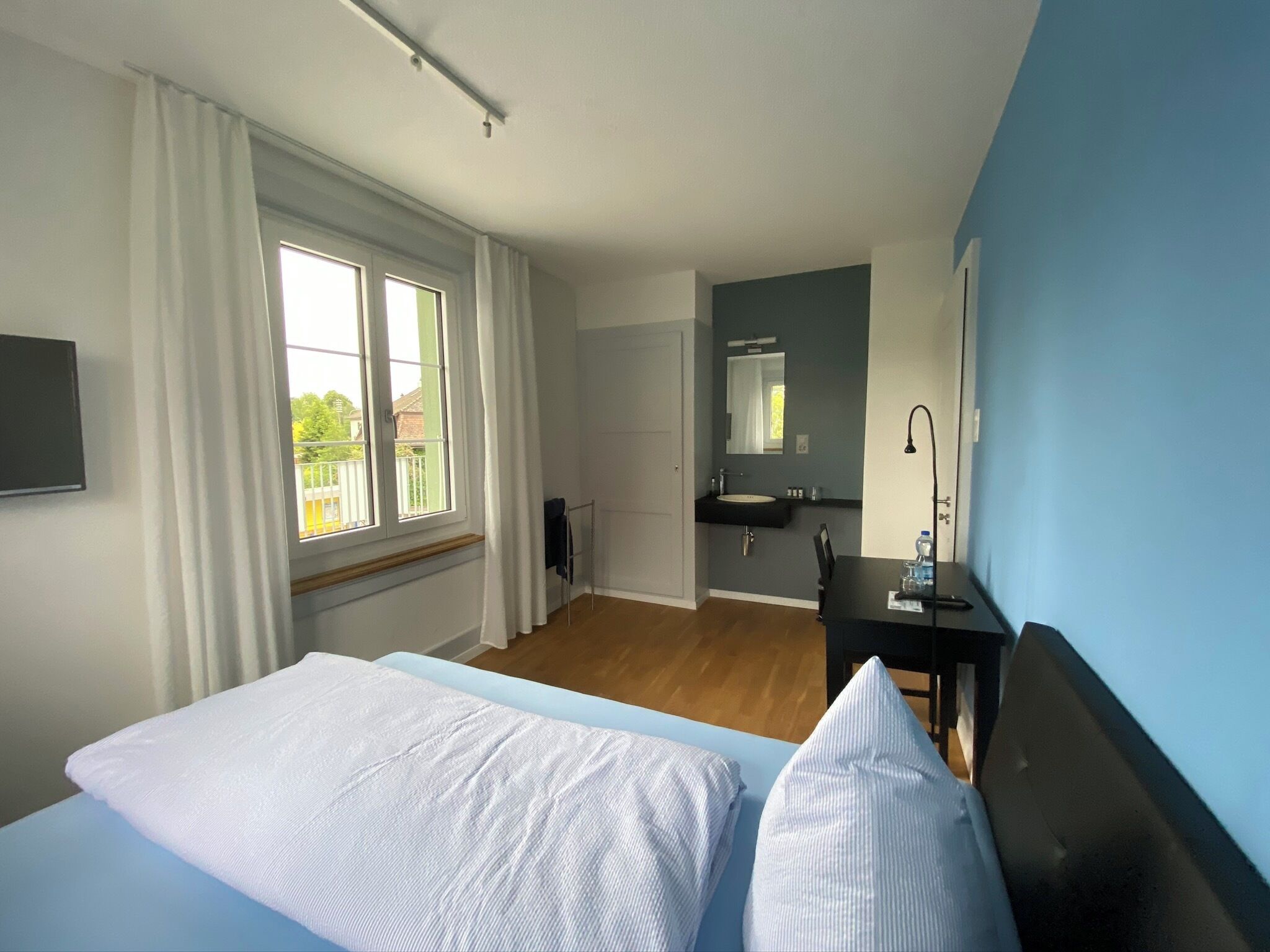 A hotel room with a bed, a desk, a mirror, and a window with curtains.