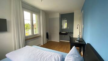 A hotel room with a bed, a desk, a mirror, and a window with curtains.