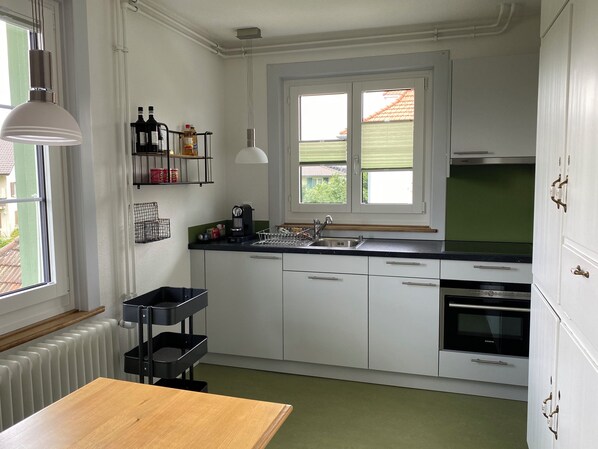 Cocina moderna con armarios blancos, encimera negra, horno empotrado y ventana con vistas al exterior.
