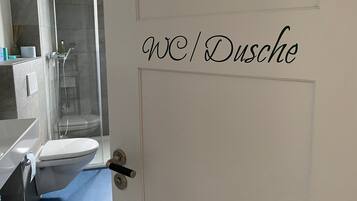 Une salle de bain avec des toilettes, une douche et une porte sur laquelle est écrit « WC/douche ».