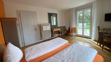 A hotel room with a bed, a desk, a chair, a radiator, a mirror, and a window.