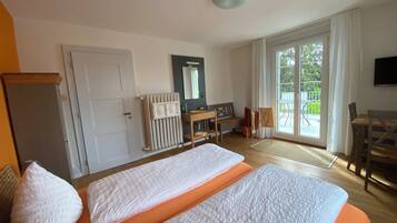 Une chambre d’hôtel avec deux lits, un bureau, une chaise, un radiateur et une vue sur l’extérieur.