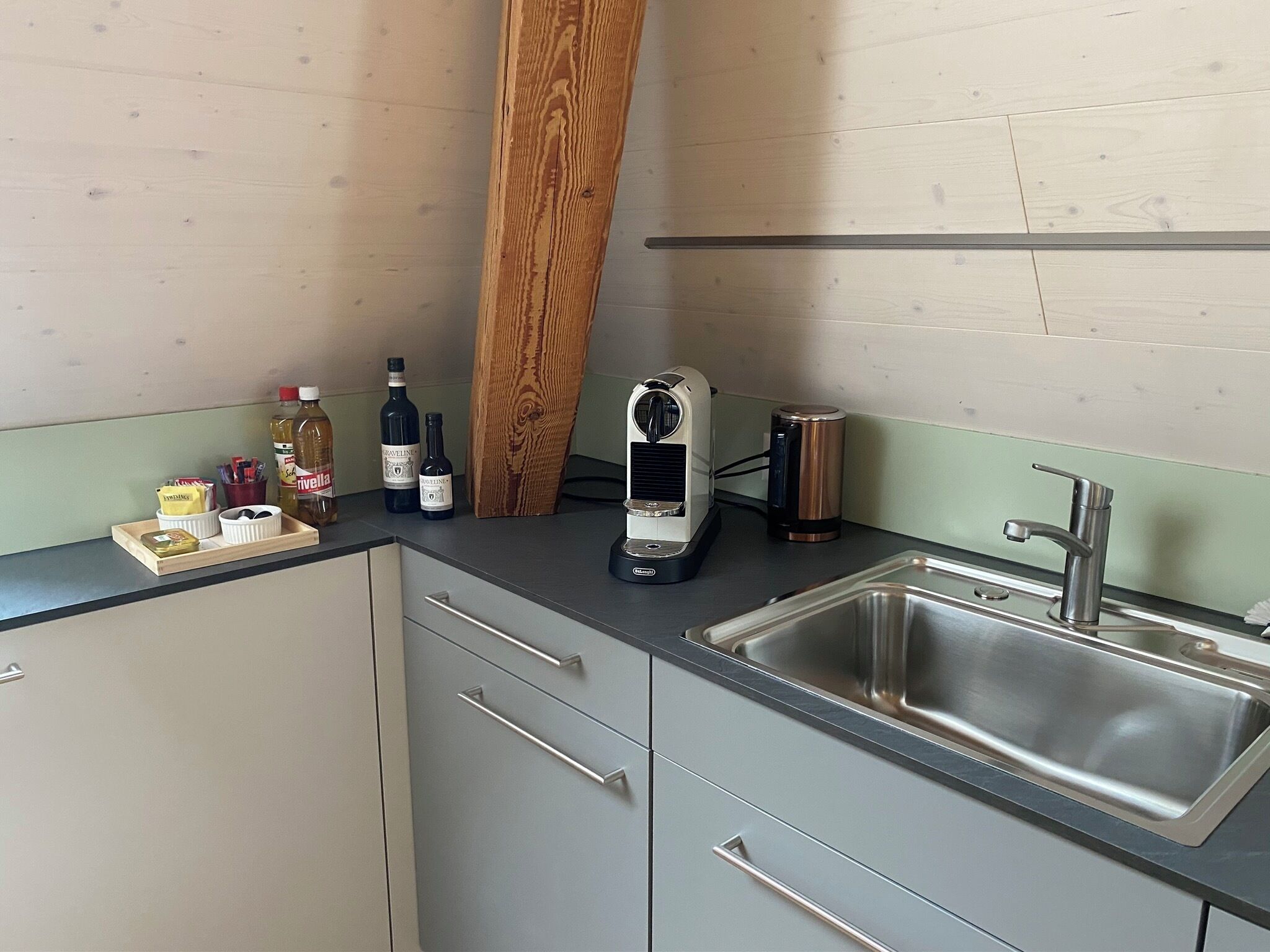 A kitchen with a stainless steel sink, wooden cabinets, a coffee maker, and various bottles on the counter.